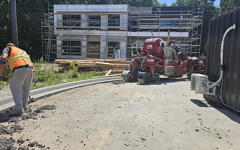 Worker operating curb machine near scaffolded home