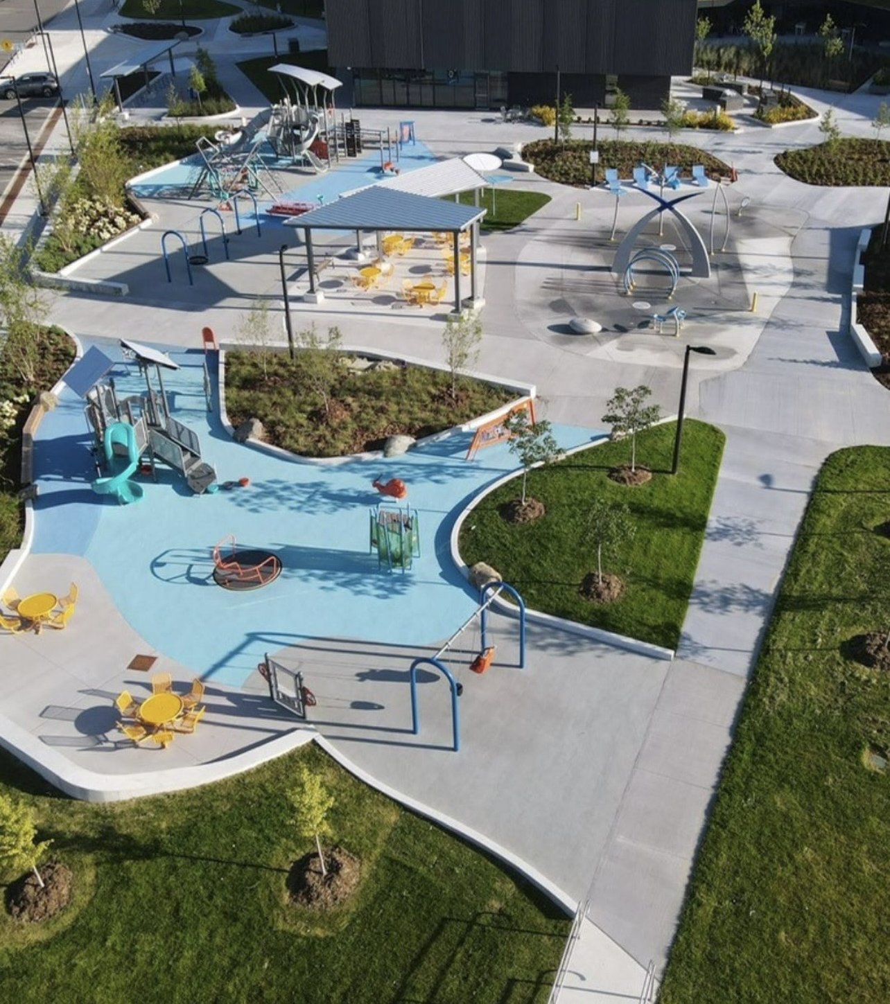 East Gwillimbury Health and Active Living Plaza – Drone view of the blue rubber playground, splash pad and shade shelters with the community centre behind