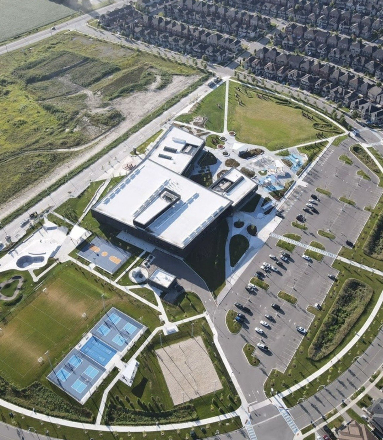 Drone view of the East Gwillimbury Health and Active Living Plaza: community centre, parking, sports fields, courts, skate park and playground with the subdivision beyond
