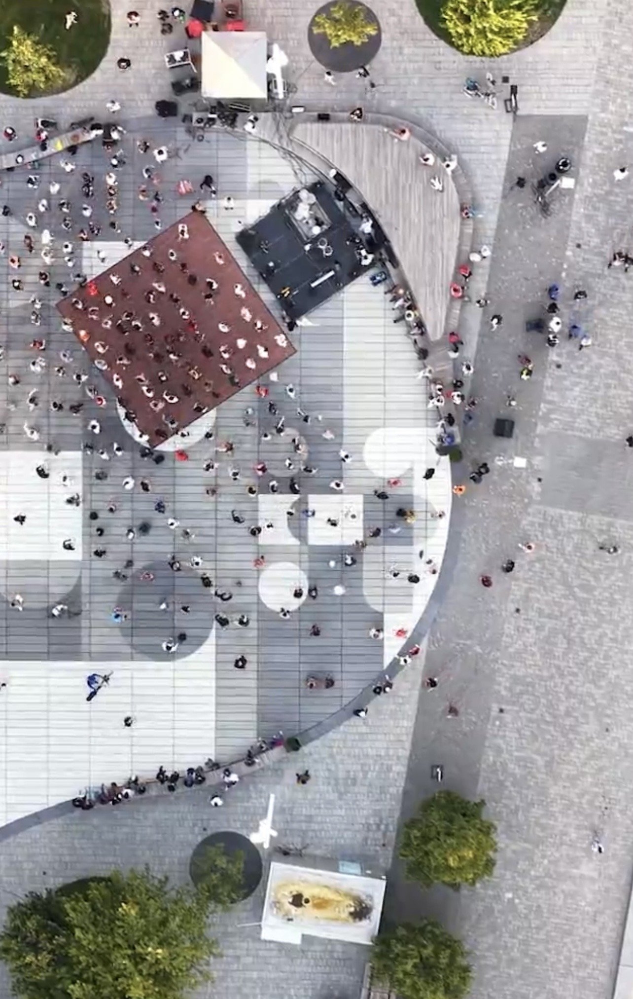 Harbourfront Centre Community Square – Drone view of the stage, curved bench edge, tree grove and crowd on the plaza