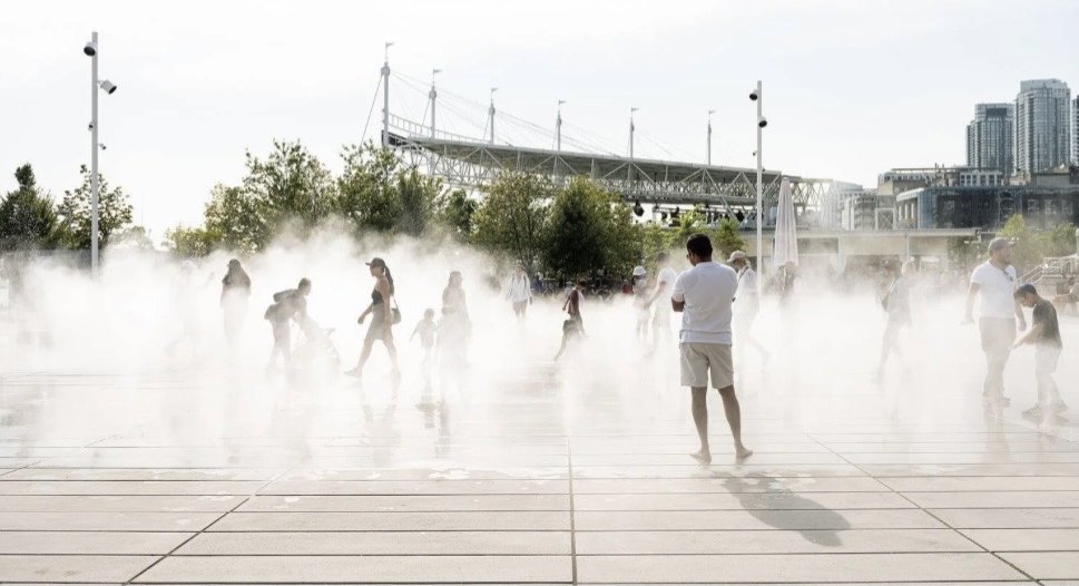 Harbourfront Centre Community Square – Visitors walking through the fog feature with the Simcoe WaveDeck and city skyline beyond