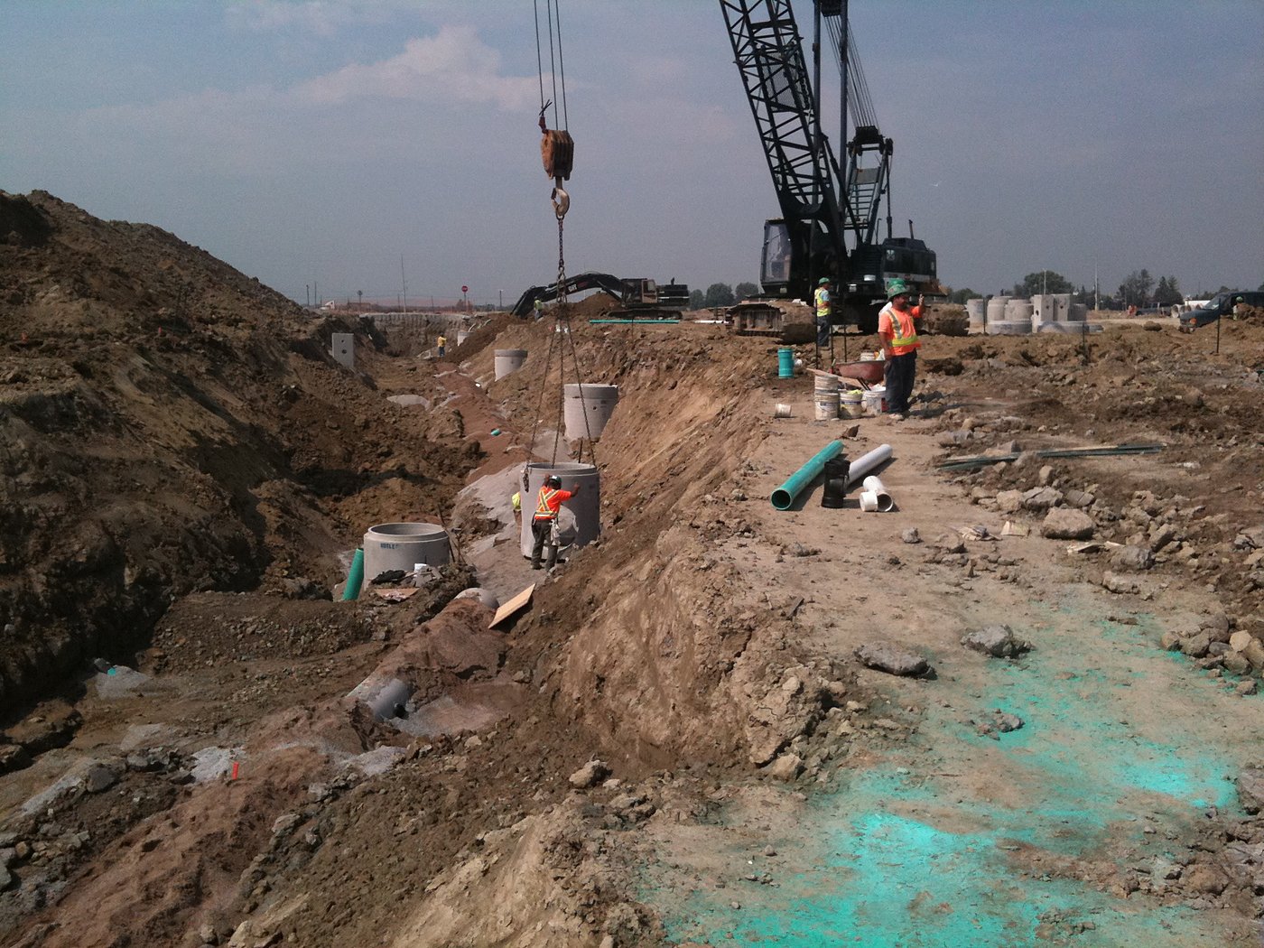 Crane lowering storm manholes into excavated trench
