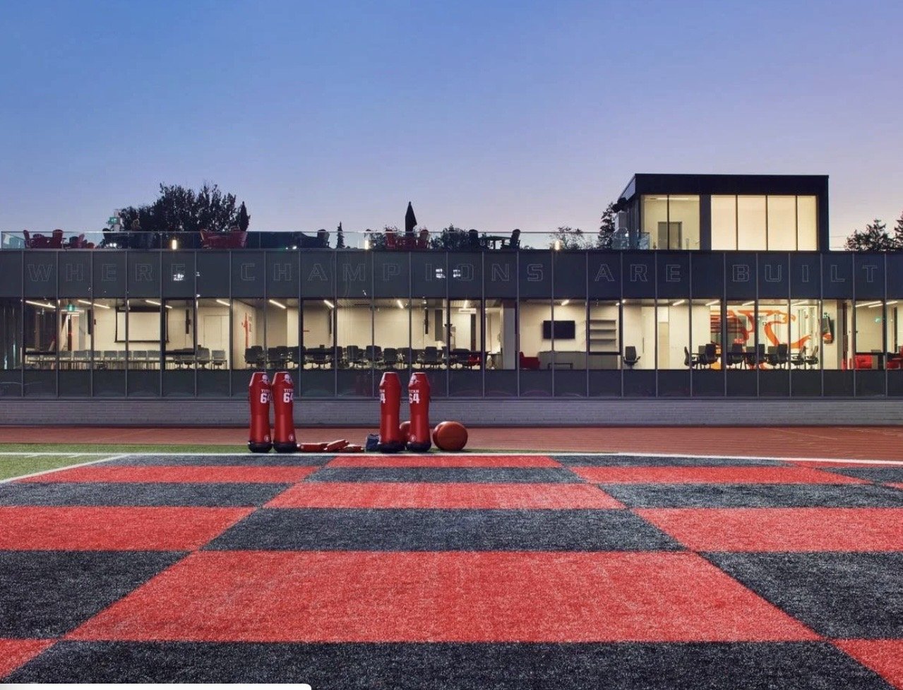 University of Guelph – Alumni Stadium – Gryphon Football Pavilion at dusk with the red and black artificial turf practice field in the foreground