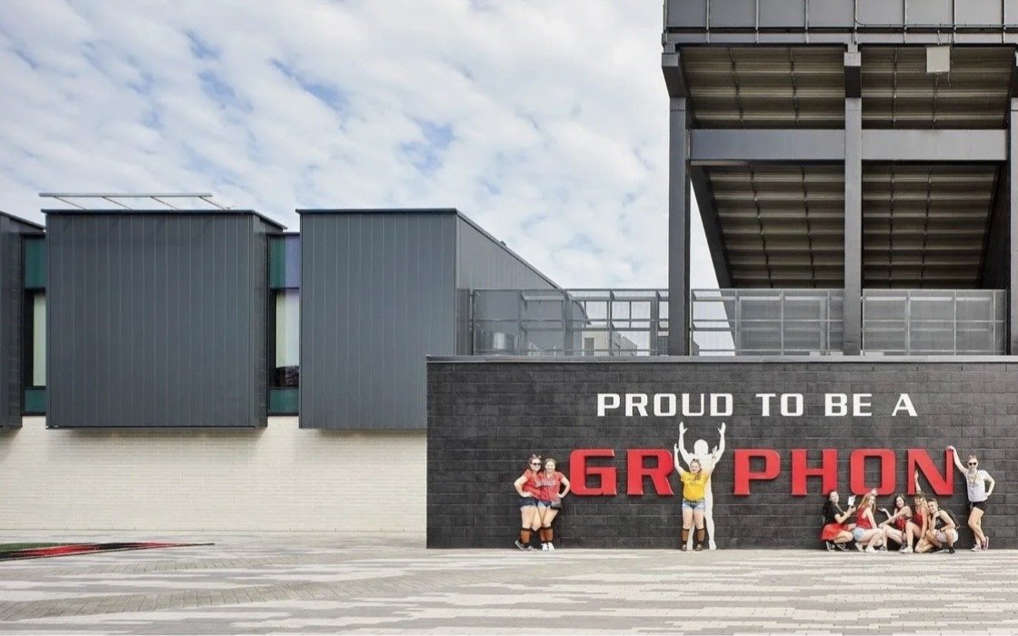 University of Guelph – Alumni Stadium – Fans posing at the Proud to be a Gryphon wall beside the pavilion and grandstand