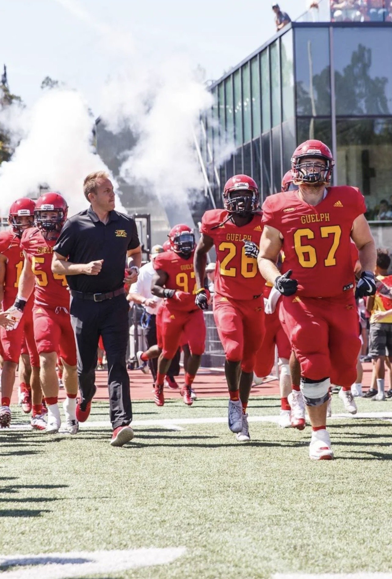 University of Guelph – Alumni Stadium – Guelph Gryphons football players running onto the turf with the pavilion behind