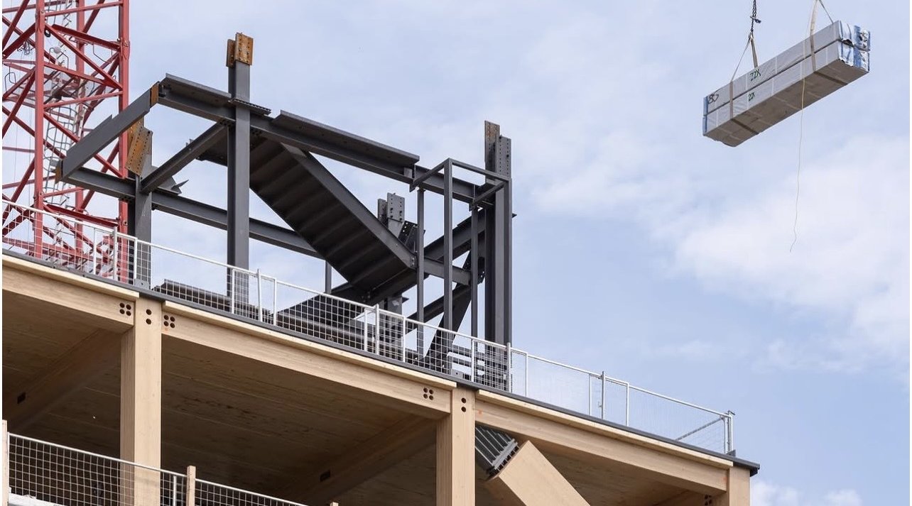 University of Toronto – Academic Tall Wood Tower – Rooftop steel framing above exposed glulam floors as a wrapped timber panel hangs from the tower crane