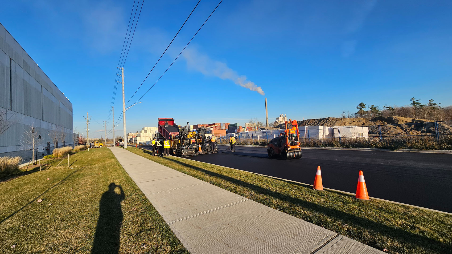 Road paving crew installing asphalt with industrial buildings